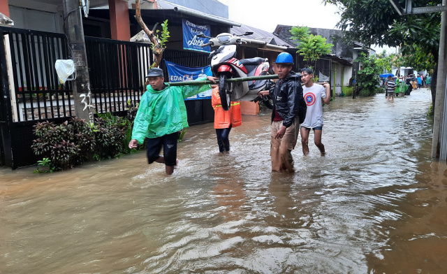 Warga memikul sepeda motor melewati banjir di Kompleks Baruga 2, Malassar.