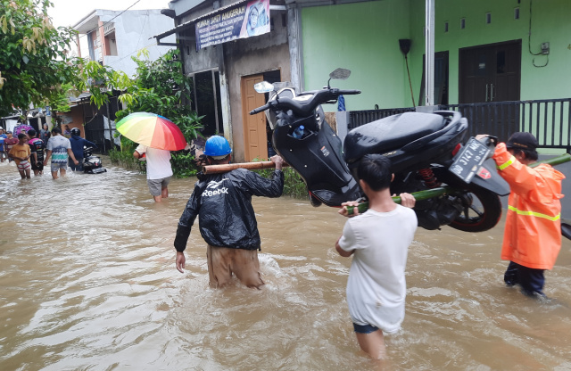 Warga memikul sepeda motor melewati banjir di Kompleks Baruga 2, Malassar.