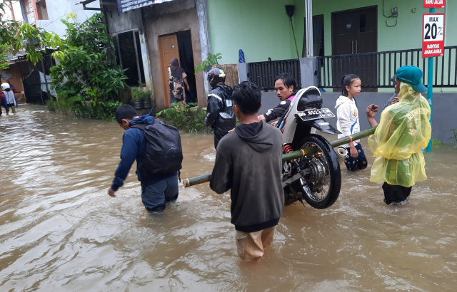 Warga memikul sepeda motor melewati banjir di Kompleks Baruga 2, Malassar.