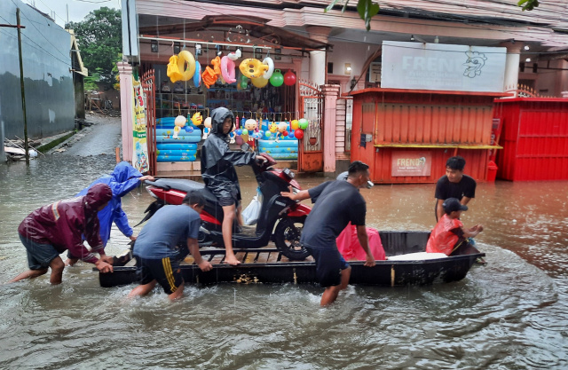 Warga menggunakan perahu untuk melewati jalan yang terendam banjir di Jalan Nipa-nipa, Makassar.