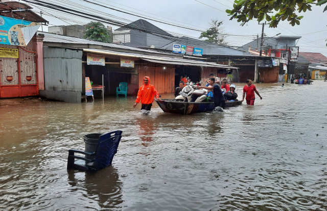 Warga menggunakan perahu untuk melewati jalan yang terendam banjir di Jalan Nipa-nipa, Makassar.