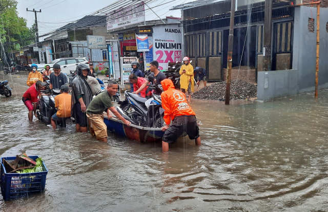 Warga menggunakan perahu untuk melewati jalan yang terendam banjir di Jalan Nipa-nipa, Makassar.