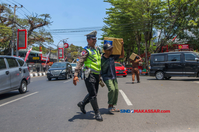 Sejumlah warga menyebrangi jalanan sembari membawa bantuan sembako gratis di Makassar, Kamis (14/9/2023). 