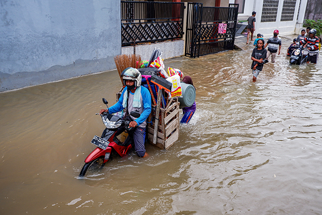 Pedagang keliling membawa jualannya melewati banjir di Kelurahan Manggala, Makassar, (28/12/2022).