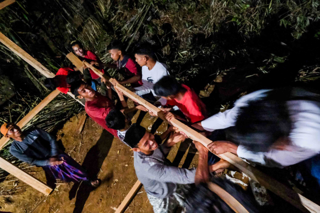 Warga bergotong royong mendirikan rumah kayu pada malam hari di Dusun Cindakko, Kabupaten Maros, Sulawesi Selatan, (4/11/2023).