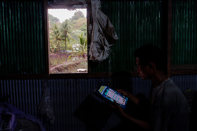 Sunardi (35) melihat informasi kemudahan menggunakan aplikasi PLN Mobile saat beristirahat di Rumah Produksi Penggilingan Padi Listrik di Kampung Massaloeng, Rammang-Rammang, Desa Salenrang, Kec.Bontoa, Kabupaten Maros, Sulawesi Selatan, Sabtu (25/11/2023).