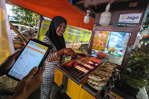 Pedagang Pisang Epe tengah membuka aplikasi keuangan digital Jago  di Kawasan Kuliner Pantai Losari, Makassar (10/2/2024). Foto: SINDO Makassar/Muchtamir Zaide