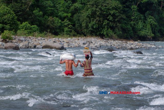 Warga membawa telur dan ikan dari pasar saat melintasi derasnya arus sungai di Desa Bonto Matinggi, Kecamatan Tompobulu, Kabupaten Maros, Sulsel, Kamis (15/02/2024).