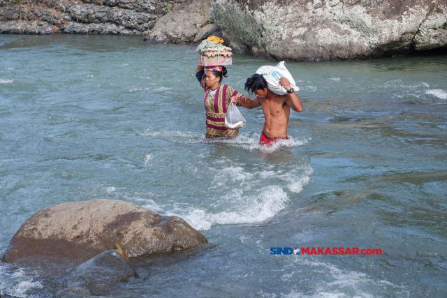 Warga membawa telur dan ikan dari pasar saat melintasi derasnya arus sungai di Desa Bonto Matinggi, Kecamatan Tompobulu, Kabupaten Maros, Sulsel, Kamis (15/02/2024).