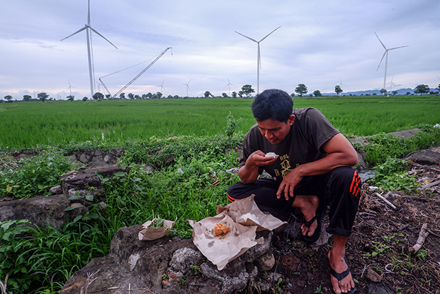 Seorang petani beristirahat sejenak sambil menikmati hidangan di tengah hamparan sawahnya setelah seharian bekerja