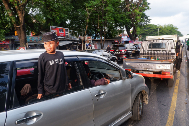 Seorang anak terlihat keluar melalui jendela mobil karena terjebak lama dalam kemacetan.