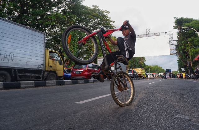 Seorang anak memanfaatkan kondisi jalan yang lengang untuk bermain sepeda dengan leluasa.