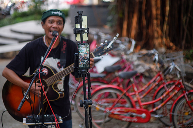 Seorang pengamen jalanan di Kota Makassar tampil penuh semangat di depan kamera ponsel untuk siaran langsung di TikTok.