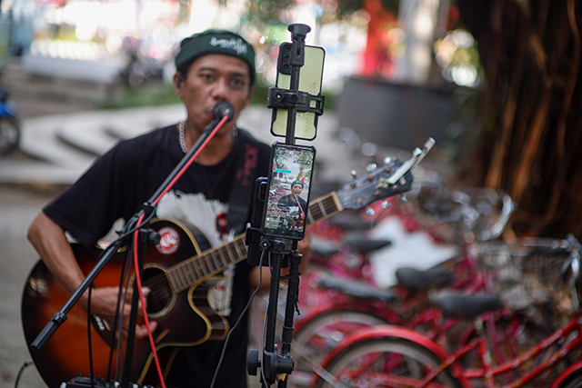 Seorang pengamen jalanan di Kota Makassar tampil penuh semangat di depan kamera ponsel untuk siaran langsung di TikTok.