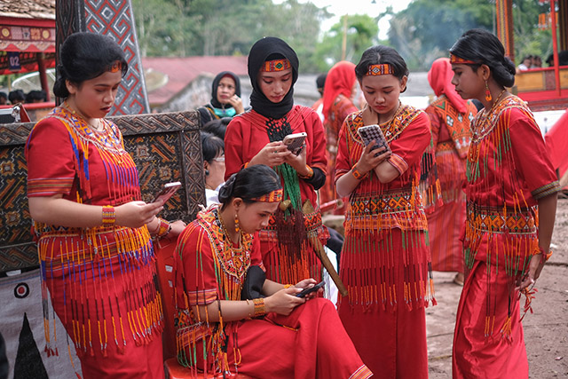 Sejumlah pemudi Toraja mengenakan busana adat merah khas Toraja tampak asyik menggunakan smartphone saat menghadiri prosesi adat Rambu Solo di Toraja.