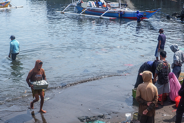 Seorang nelayan memanggul keranjang berisi ikan segar menuju area pelelangan di TPI Beba, Takalar, sementara warga lainnya menunggu hasil tangkapan didaratkan. Aktivitas ini menjadi bagian penting dari denyut ekonomi pesisir yang berlangsung setiap hari.
