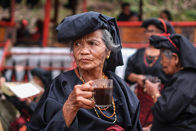 Seorang perempuan lanjut usia mengenakan busana adat khas Toraja menikmati kopi hitam di sela-sela prosesi Rambu Solo di Kabupaten Tana Toraja, Sulawesi Selatan.