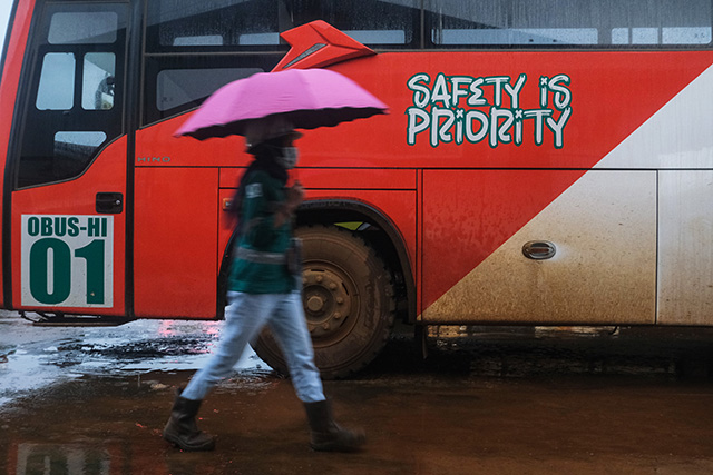 Seorang pekerja melintas sambil membawa payung di depan bus karyawan bertuliskan 'Safety is Priority' di area operasional Harita Nickel, Pulau Obi, Maluku Utara, Selasa (16/9/2025).
