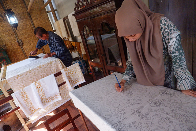 Seorang perajin muda menggambar pola batik di kain mori, sementara Sukadi, perajin senior Batik Gunasti di Kampung Batik Kauman, Solo, mencetak motif menggunakan cap tembaga.