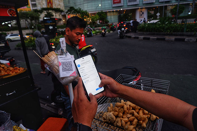 Seorang pembeli melakukan pembayaran nontunai menggunakan QRIS AstraPay saat bertransaksi dengan pedagang kaki lima di Jakarta, Kamis (27/11/2025).