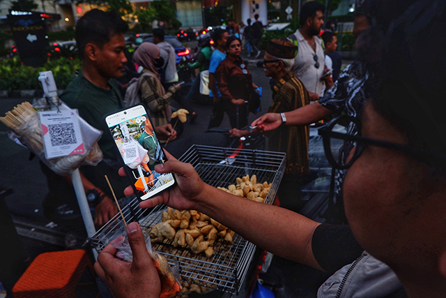 Seorang pembeli melakukan pembayaran nontunai menggunakan QRIS AstraPay saat bertransaksi dengan pedagang kaki lima di Jakarta, Kamis (27/11/2025).
