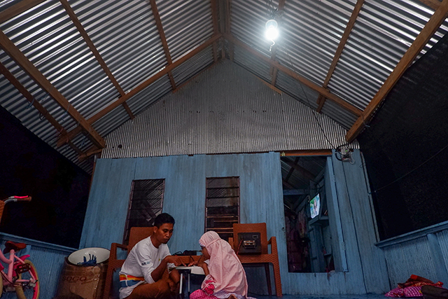 Sunardi menemani anaknya belajar di bawah cahaya lampu listrik di rumah panggungnya. Kehadiran listrik dan perahu listrik bantuan PLN kini semakin memudahkan aktivitas harian masyarakat di kawasan karst Rammang-Rammang.