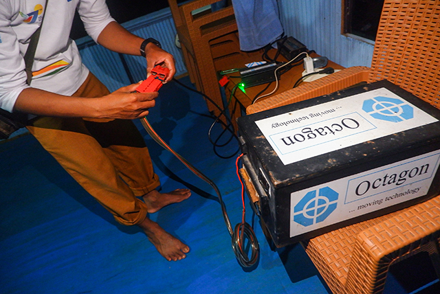 Sunardi menghubungkan baterai ke alat pengisi daya di rumahnya di Desa Berua, Rammang-Rammang. Pengisian rutin ini memastikan perahu listrik bantuan PLN siap digunakan setiap hari untuk kebutuhan warga.