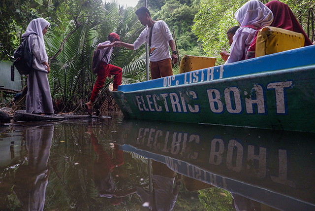 Anak-anak sekolah dibantu menaiki perahu listrik bantuan PLN di Desa Berua, Rammang-Rammang. Perahu ramah lingkungan ini menjadi sarana transportasi utama warga untuk beraktivitas di jalur sungai.