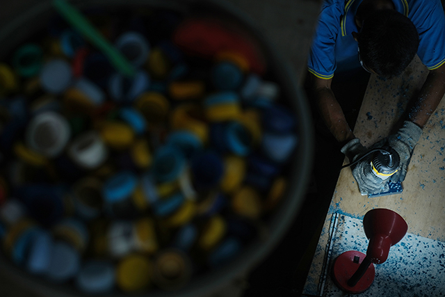 Seorang pekerja mengolah tutup botol plastik di rumah produksi Rappo Indonesia, bagian dari program TJSL PLN yang mendaur ulang sampah menjadi produk bernilai ekonomi.