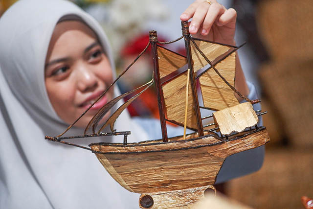 Seorang perajin dari Komunitas Pemberdayaan Kasih Bunda memperlihatkan miniatur perahu phinisi berbahan eceng gondok kering yang dihasilkan di rumah produksi Sambung Jawa, Makassar.