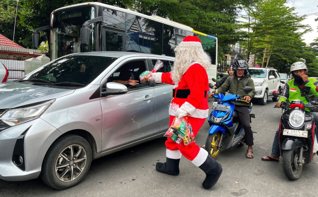 Seorang pria berkostum Santa Claus membagikan bingkisan Natal kepada para pengendara yang melintas di Jalan Botolempangan, Makassar.