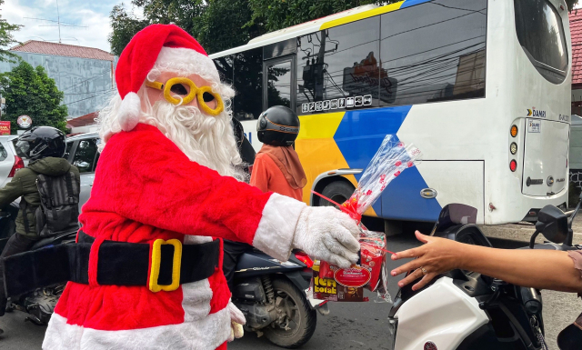 Seorang pria berkostum Santa Claus membagikan bingkisan Natal kepada para pengendara yang melintas di Jalan Botolempangan, Makassar.