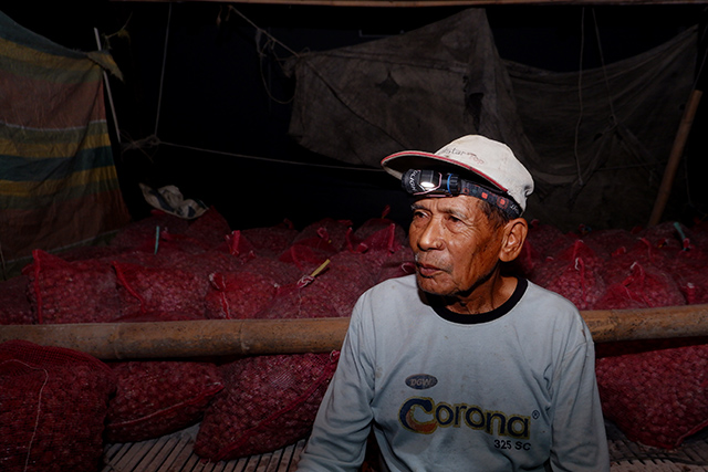 Petani bawang merah Usman (68) beristirahat di dekat tumpukan hasil panen yang telah dikemas di Kabupaten Enrekang.