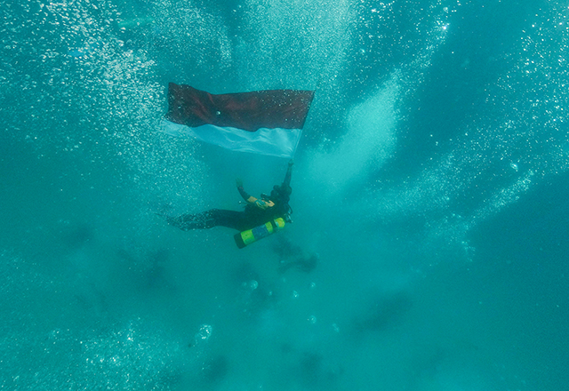 Penyelam menyambut Hari Ulang Tahun (HUT) ke-81 Republik Indonesia dengan mengibarkan bendera Merah Putih di dasar laut perairan Pulau Samalona.
