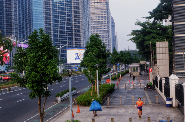 Seorang warga berolahraga di trotoar, sementara warga lainnya membawa barang dan menjalani aktivitas mencari nafkah di kawasan Senayan, Jakarta.