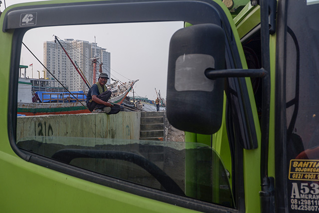 Seorang buruh beristirahat di tepi dermaga yang dipenuhi kapal kayu di Pelabuhan Sunda Kelapa, Jakarta.