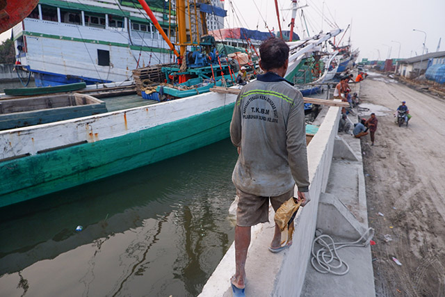 Seorang buruh berjalan di tepi kapal kayu yang bersandar di Pelabuhan Sunda Kelapa, Jakarta.