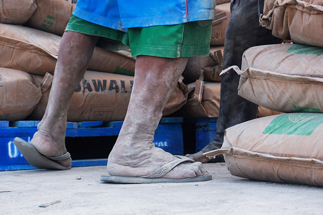 Kaki yang berdebu dan karung-karung semen menjadi bagian dari keseharian pekerja yang tetap berjuang mencari nafkah di tengah cuaca panas musim kemarau.